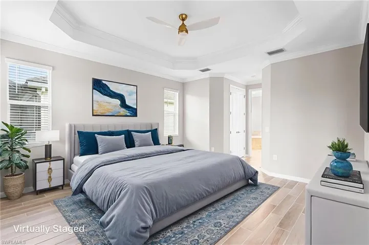 Bedroom with a raised ceiling, light wood-style floors, multiple windows, and ornamental molding