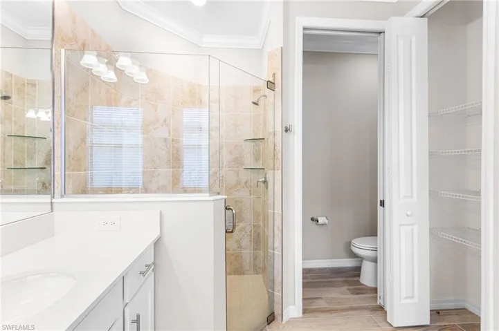 Full bathroom featuring vanity, a shower stall, crown molding, a spacious closet, and wood finished floors