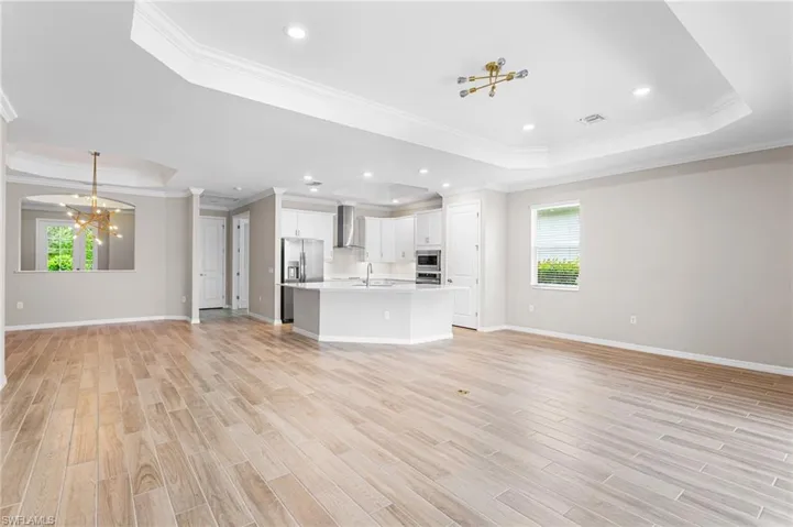 Unfurnished living room featuring a raised ceiling, a chandelier, crown molding, healthy amount of natural light, and light wood-style floors