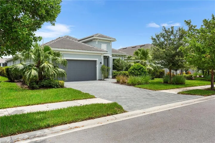 View of front of home featuring an attached garage, a tile roof, decorative driveway, and a front lawn