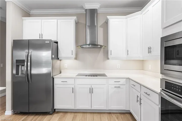 Kitchen with appliances with stainless steel finishes, wall chimney exhaust hood, white cabinetry, light wood-style floors, and crown molding
