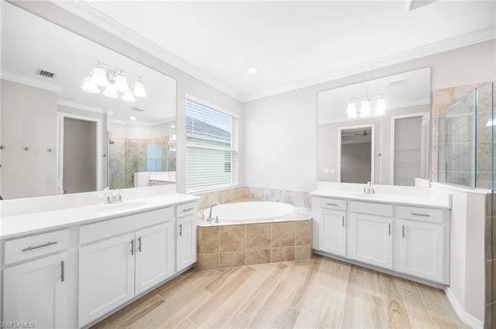 Bathroom featuring two vanities, tiled shower, a bath, ornamental molding, and wood finished floors
