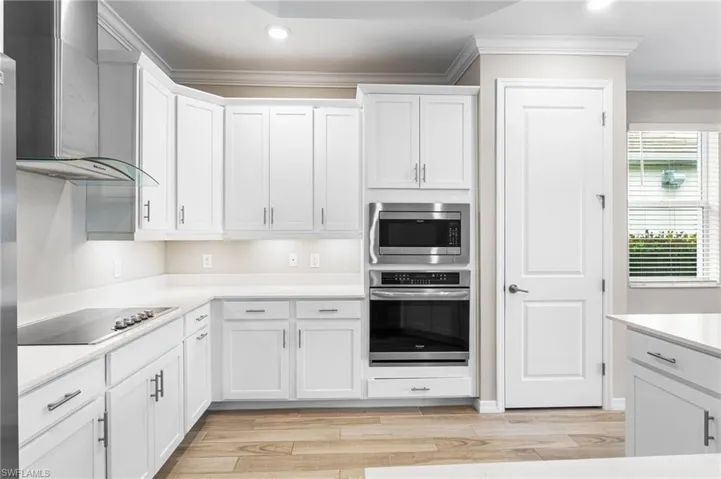 Kitchen with crown molding, wall chimney exhaust hood, stainless steel appliances, recessed lighting, and white cabinetry