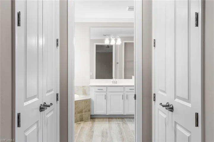 Full bathroom featuring vanity, crown molding, a bath, wood finished floors, and a chandelier