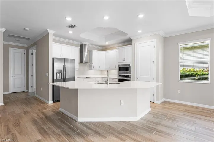 Kitchen with stainless steel appliances, light wood-style flooring, light countertops, crown molding, and a kitchen island with sink
