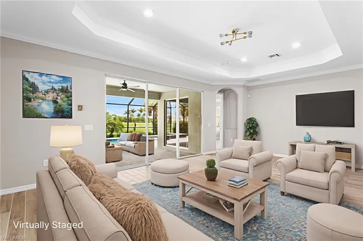 Living area with a tray ceiling, wood finished floors, arched walkways, crown molding, and ceiling fan