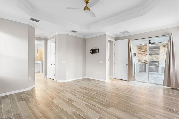 Spare room with a tray ceiling, a ceiling fan, light wood finished floors, and crown molding