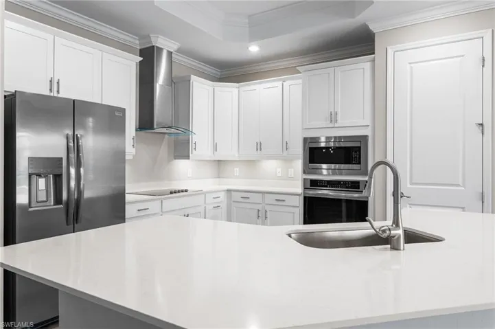 Kitchen with appliances with stainless steel finishes, ornamental molding, wall chimney range hood, recessed lighting, and light countertops