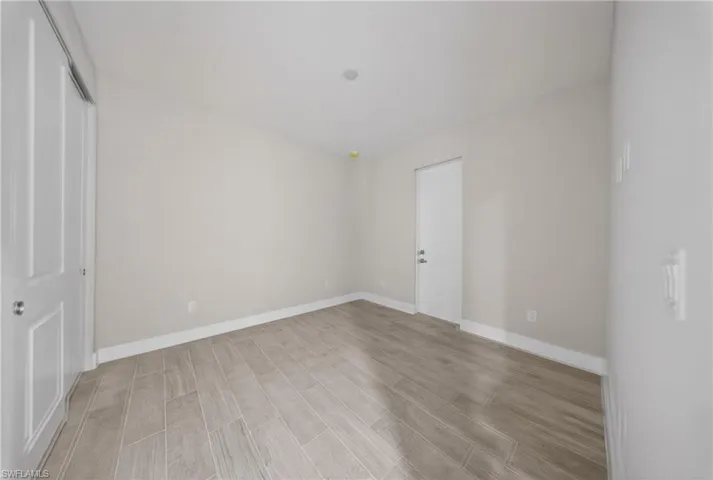 Spacious room featuring wood-look tile flooring, light neutral wall paint, white baseboards, and a recessed ceiling light