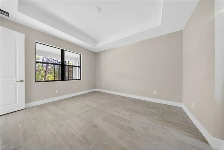Spacious room featuring wood-finish tile flooring, a tray ceiling, and a large window with black framing