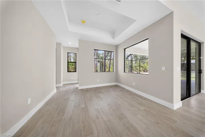 Spacious interior featuring wood-finish tile flooring, tray ceiling, multiple windows with black framing, and a large sliding glass door