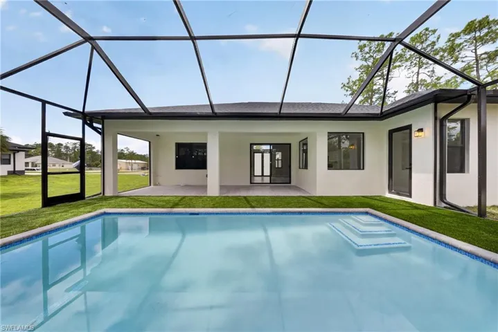 Screened-in swimming pool area featuring a rectangular pool with integrated steps, surrounded by artificial turf and a covered patio