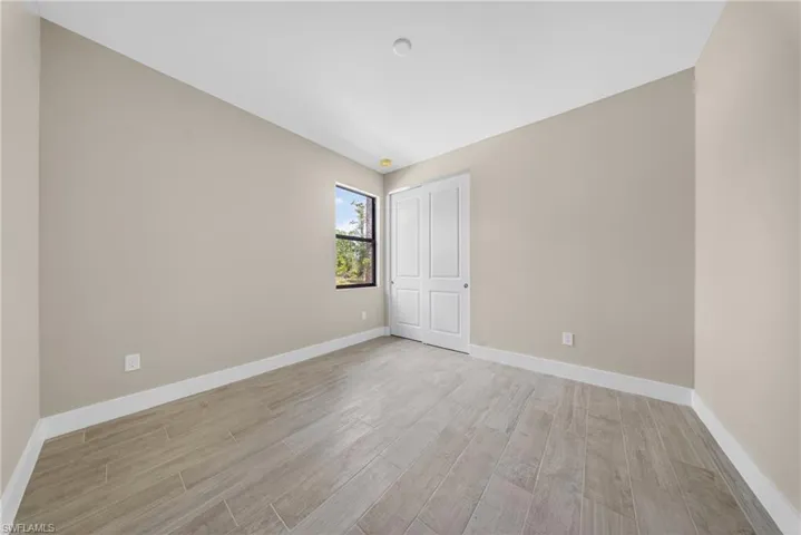 Neutral-toned room featuring plank-style tile flooring, a single window with a dark frame, and bi-fold closet doors