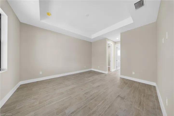 Spacious room featuring wood-finish tile flooring, neutral wall tones, white baseboards, and a tray ceiling