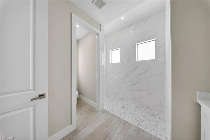 Large walk-in shower featuring two square windows, a white marble-patterned tiled wall, and a mosaic pebble floor