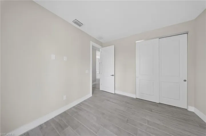 Spacious room featuring gray wood-finish tile flooring, a double-panel sliding closet door, a single-panel interior door, and light neutral wall finishes with white baseboards