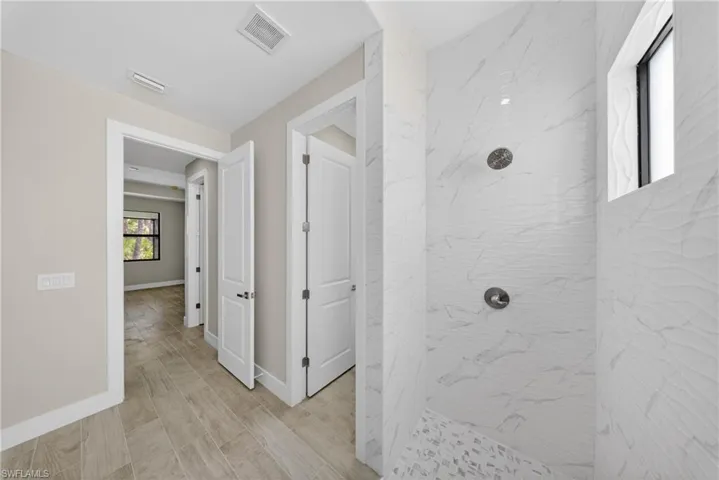 Contemporary shower enclosure featuring two shower heads, patterned white wall tiles, and mosaic tile flooring