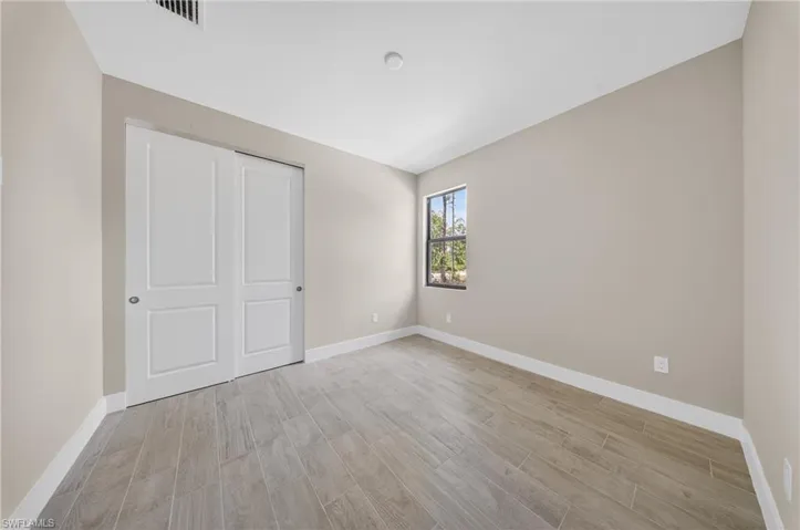 Neutral tone walls featuring wood-finish tile flooring, a double-panel bifold closet, and a single window with dark framing