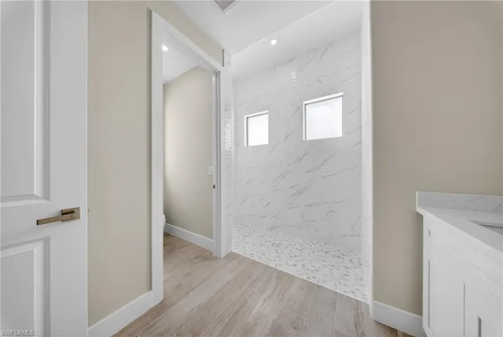 Bathroom featuring a walk-in shower with textured tile walls, two frosted windows, and a pebble-style floor