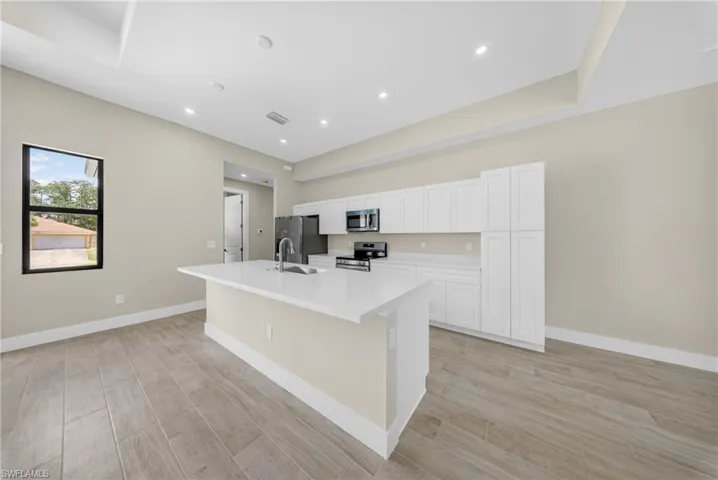 Spacious kitchen featuring an expansive central island with a sink, white cabinetry, integrated stainless-steel appliances, recessed lighting, and wood-finish flooring