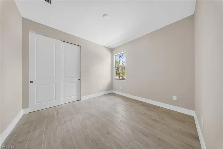 Spacious room featuring light wood-finish flooring, neutral wall paint, and white trim
