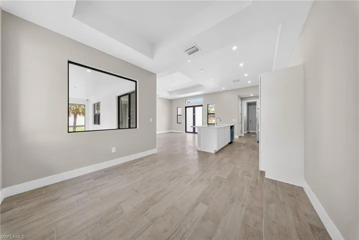 Expansive interior space featuring wood-finish flooring, recessed lighting, a tray ceiling, and a large pass-through window with black trim
