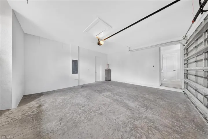 Spacious garage featuring a concrete floor, painted white walls, an attic access panel, and a visible water heater