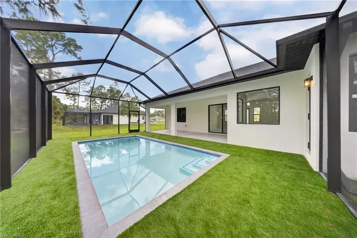 Screened pool enclosure featuring a rectangular pool with integrated steps, artificial turf, and a white stucco exterior