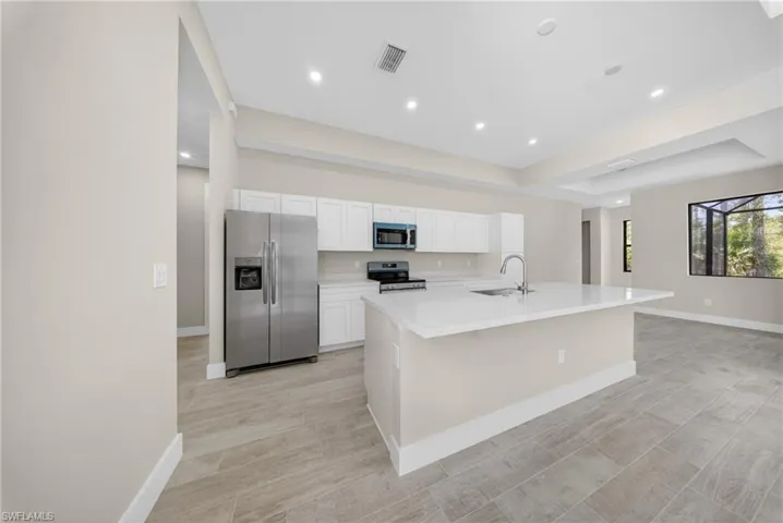 Kitchen featuring a central island with an undermount sink, stainless steel appliances, white cabinetry, and light-toned tile flooring