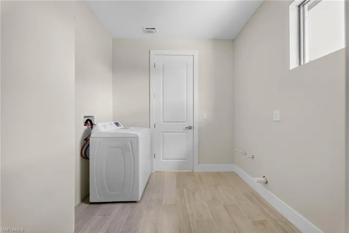 Dedicated laundry space featuring wood-finish flooring, light neutral wall paint, and white baseboards