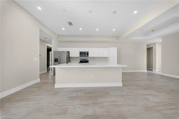 Open-concept kitchen and living area featuring a central island, recessed lighting, neutral wall tones, white cabinetry, and wood-finish tile flooring