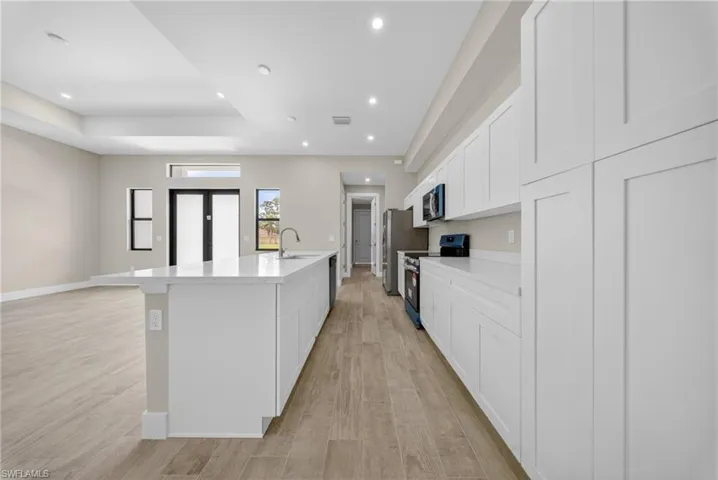 Contemporary kitchen featuring a spacious island with a built-in sink, white cabinetry, integrated appliances, recessed lighting, and wood-finish flooring
