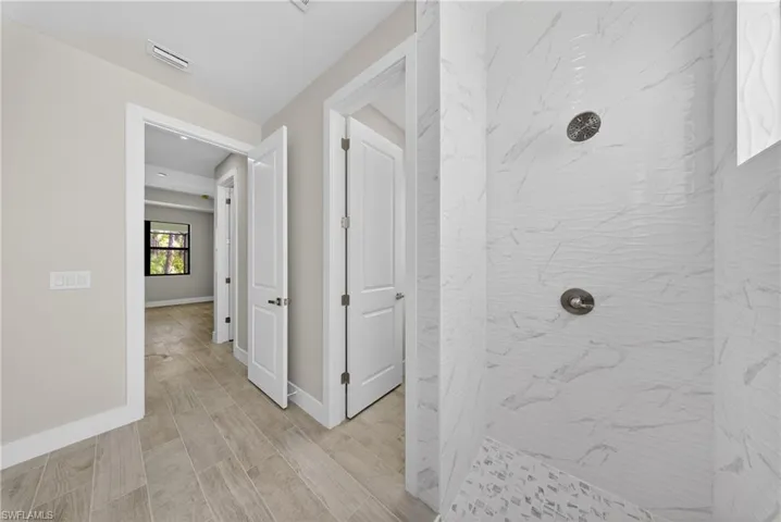 Walk-in shower featuring white marble-look wall tiles, a mosaic tile shower pan, and a brushed nickel shower head with matching controls