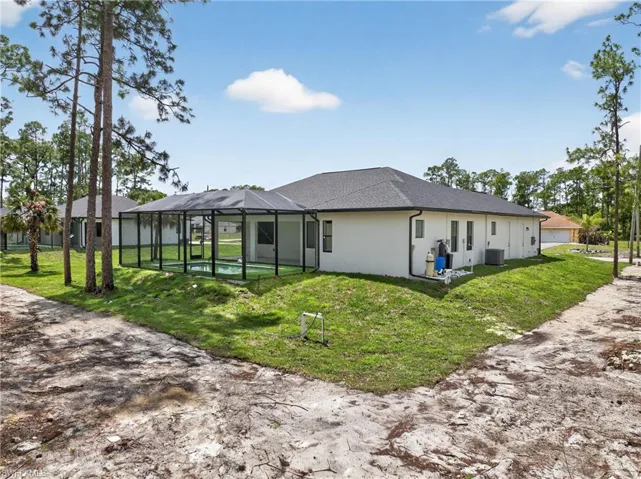 Screened lanai enclosing a pool, light stucco exterior, dark shingle roof, established trees, and a green lawn