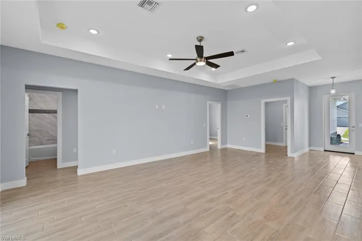 Unfurnished living room featuring visible vents, baseboards, a raised ceiling, a ceiling fan, and wood finish floors