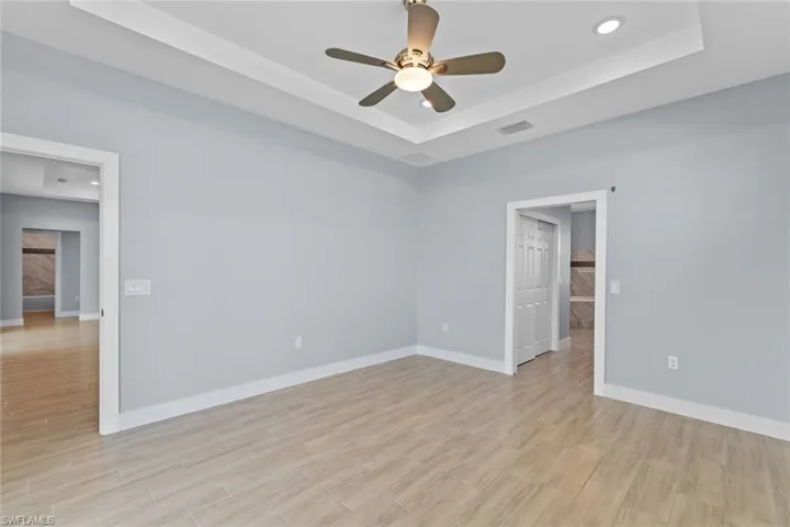 Empty room with light wood-style floors, visible vents, and a raised ceiling