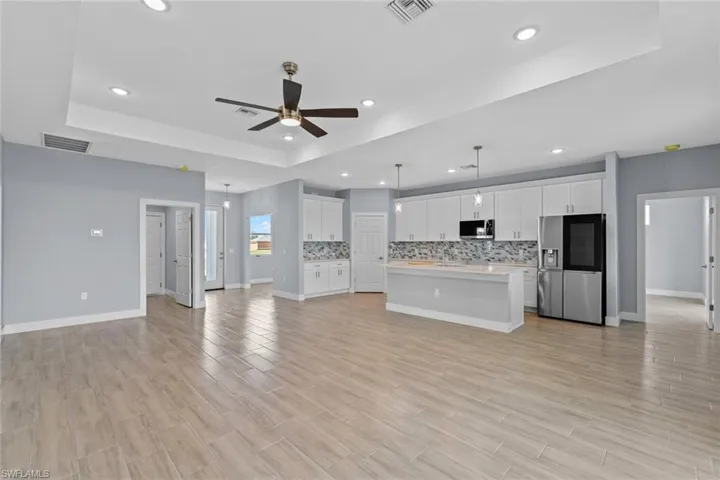 Unfurnished living room featuring light wood-style floors, visible vents, a ceiling fan, and a raised ceiling