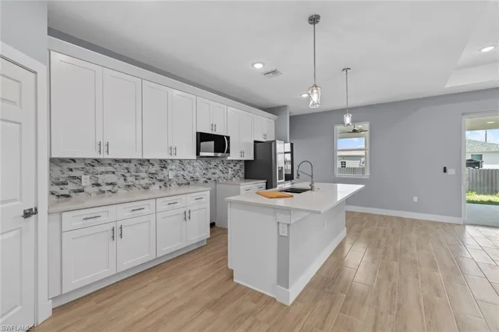 Kitchen featuring black microwave, visible vents, stainless steel refrigerator with ice dispenser, a sink, and decorative backsplash