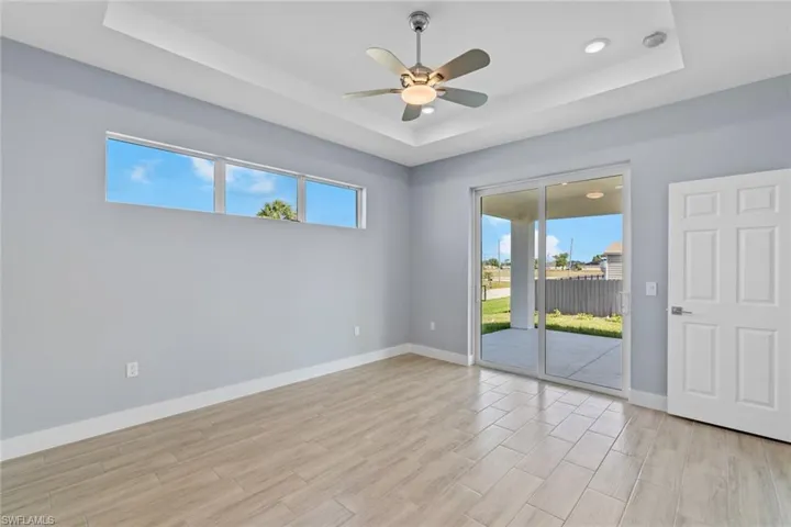 Unfurnished room featuring baseboards, light wood-style floors, a tray ceiling, and a ceiling fan
