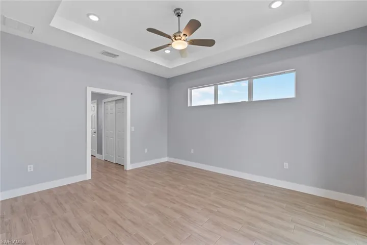 Spare room featuring a raised ceiling, baseboards, visible vents, and light wood-style flooring