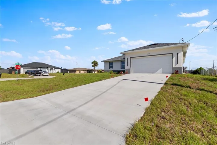 Ranch-style house with a front yard, driveway, stucco siding, and an attached garage