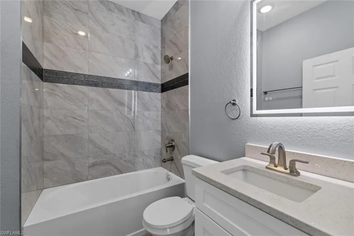 Full bath with a textured wall, shower / bath combination, vanity, and toilet