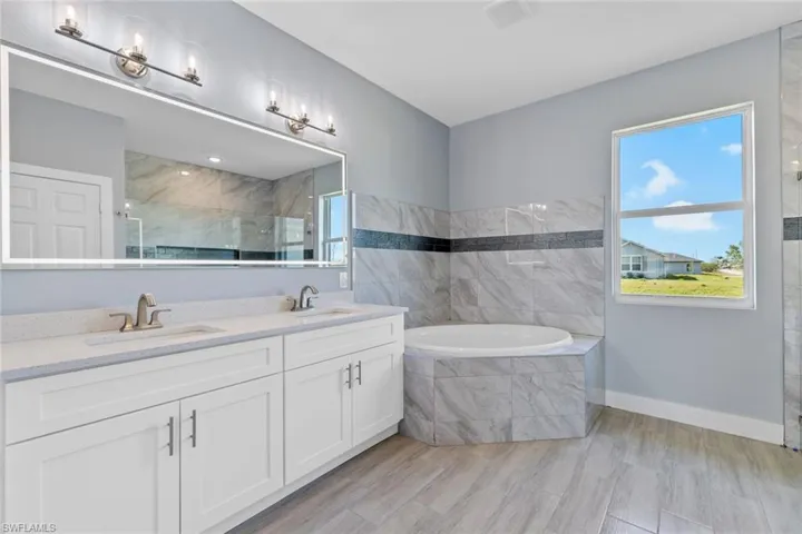Bathroom featuring tiled shower, double vanity, a garden tub, and a sink