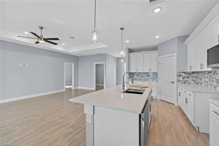 Kitchen with tasteful backsplash, a raised ceiling, a sink, ceiling fan, and a kitchen island with sink