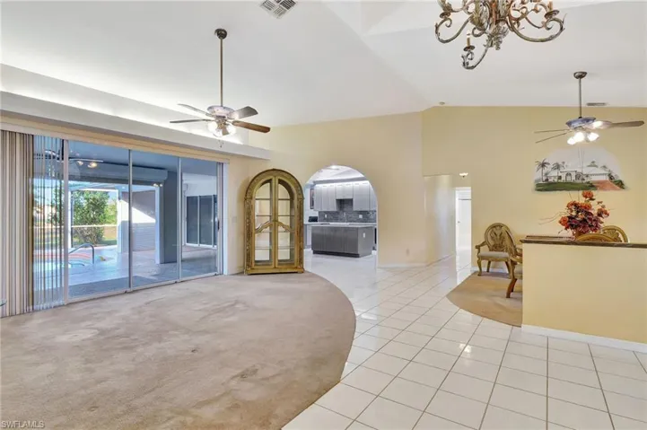 Unfurnished living room with lofted ceiling, light tile patterned floors, and ceiling fan with notable chandelier