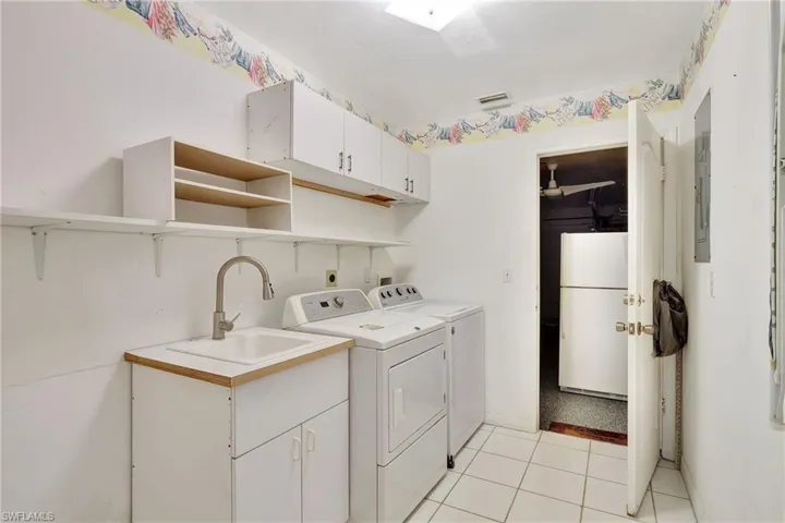 Laundry area with cabinets, light tile patterned floors, washer and dryer, and sink