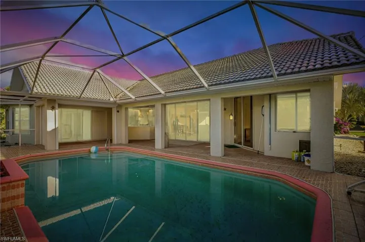 Pool at dusk with glass enclosure and a patio