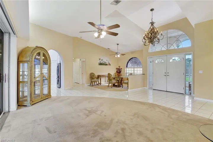 Foyer entrance featuring light tile patterned floors, ceiling fan with notable chandelier, and high vaulted ceiling