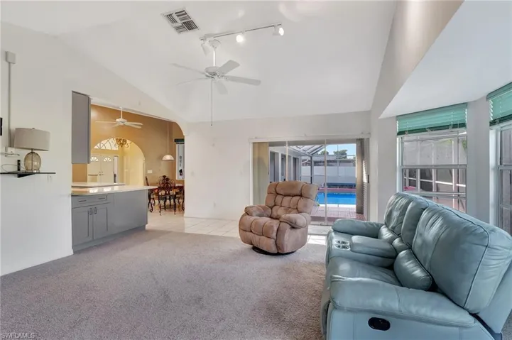 Carpeted living room with ceiling fan and vaulted ceiling