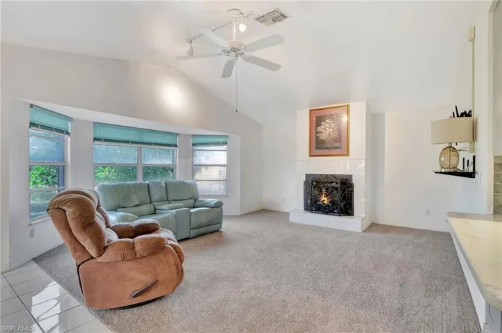 Living room featuring a tile fireplace, ceiling fan, light carpet, and vaulted ceiling